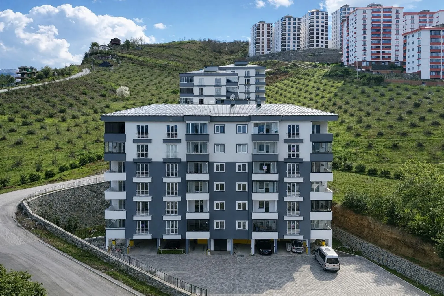 Yamaç önünde lacivert ve beyaz cepheli apartman, altında otopark